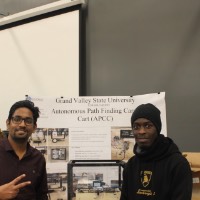 Two students standing next to an autonomous path finding cart.